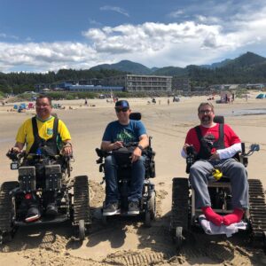 Three men with disabilities sitting in their own David's Chair on the beach