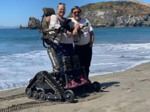 A woman standing tall in a David's chair next to a man on the beach