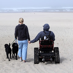West's life after spinal cord injury - West, in TrackChair, holds hands with his wife on the beach. They are accompanied by their two dogs.